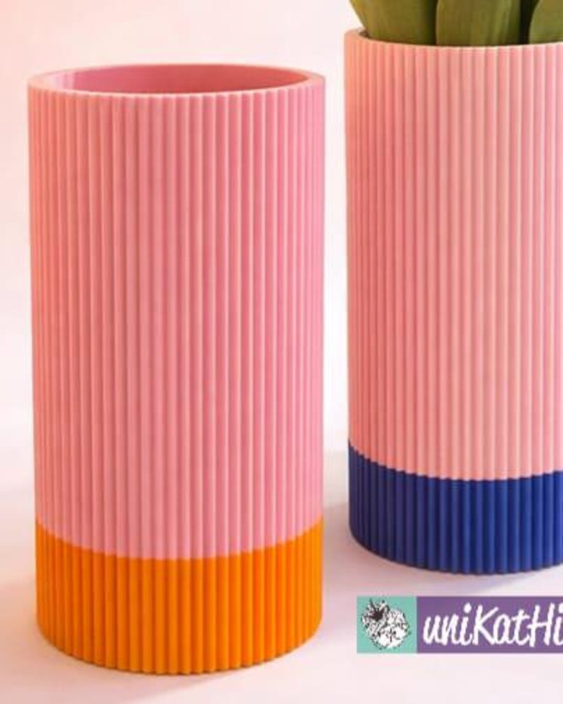 May include: Two cylindrical planters with vertical ribbed texture. One is pink with an orange base, the other is pink with a blue base. The planters are empty and ready for plants. The planters are a modern home decor item.
