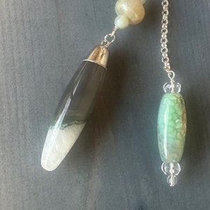 May include: A silver chain with a green and white agate pendulum and a green and white agate bead. The pendulum is attached to the chain with a silver ring. The bead is attached to the chain with a silver ring and a clear crystal bead.