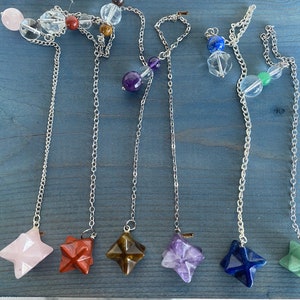 May include: Set of seven crystal pendulums with different colored stones and silver chains. The stones include rose quartz, red jasper, tiger's eye, amethyst, lapis lazuli, and green aventurine.