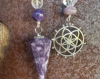May include: Two purple crystal pendulums with silver chains and decorative beads. One pendulum is a faceted point, the other has a silver flower of life charm. The beads are clear and purple.