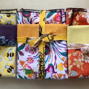May include: Four sets of fabric squares tied with a ribbon. The squares are in different patterns, including bees, flowers, and leaves. The fabric is a mix of yellow, purple, orange, and white.