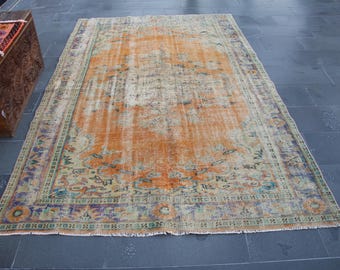 May include: A vintage rug with a faded orange background and a multi-colored floral pattern. The rug has a fringed edge and a worn, distressed look.