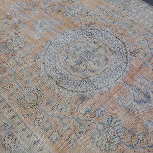 May include: A vintage rug with a faded peach background and intricate floral patterns in shades of blue and gray. The rug features a large central medallion with a geometric design.