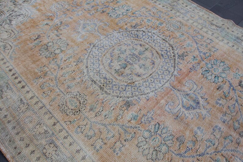 May include: A vintage rug with a faded peach background and intricate floral patterns in shades of blue and gray. The rug features a large central medallion with a geometric design.