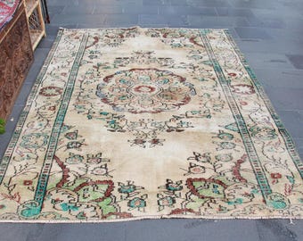 May include: A rectangular, vintage-style rug with a cream-colored central field. The rug features a central medallion and floral patterns in shades of red, green, and blue. The border is a darker green with floral motifs. The rug is placed on a dark gray tiled floor.