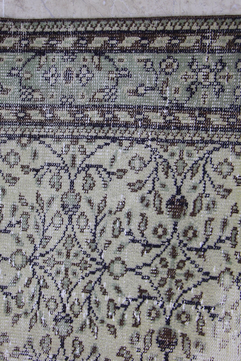 Puede incluir: Primer plano de una alfombra beige con un patr&oacute;n floral. La alfombra tiene un borde marr&oacute;n oscuro con un dise&ntilde;o geom&eacute;trico.