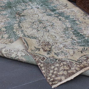 May include: A vintage rug with a faded floral pattern in shades of green, brown, and beige. The rug is folded in half, revealing the underside.