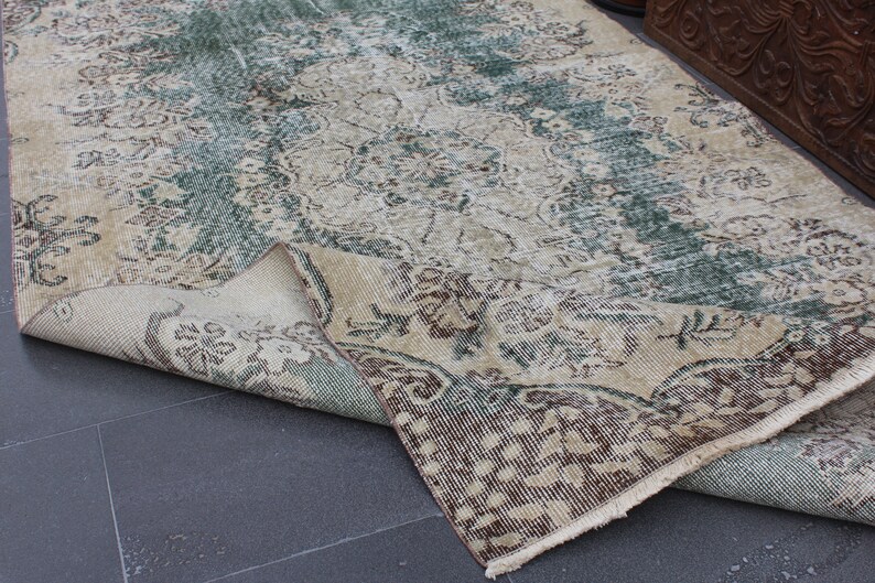 May include: A vintage rug with a faded floral pattern in shades of green, brown, and beige. The rug is folded in half, revealing the underside.