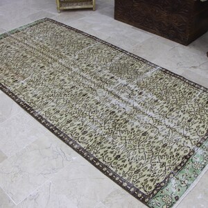 May include: A vintage style rug with a cream background and a brown and green geometric pattern. The rug has a distressed look and is perfect for adding a touch of bohemian style to any room.