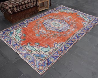 May include: Rectangular, distressed orange rug with a central floral medallion in blue and white. The rug features a blue border with floral and paisley designs, adding a vintage aesthetic. The rug is suitable for living rooms and bedrooms.