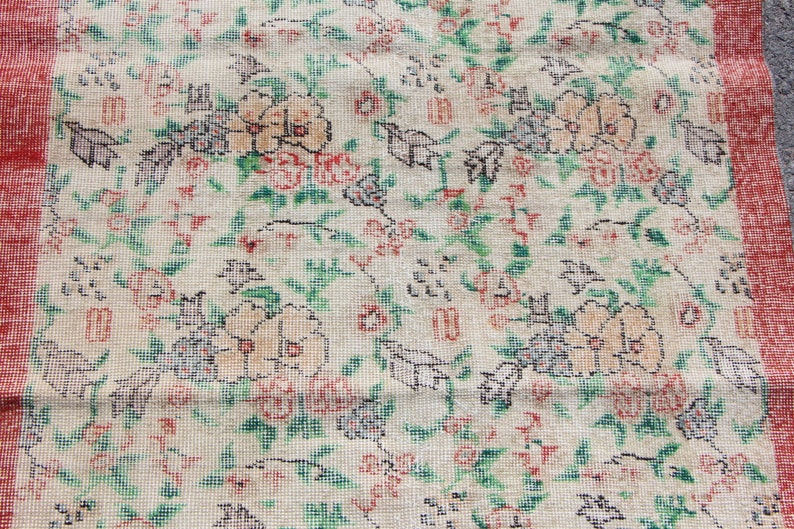 Puede incluir: Una alfombra vintage con un patr&oacute;n floral en tonos rojos, verdes y blancos. La alfombra tiene un fondo crema y un borde rojo.