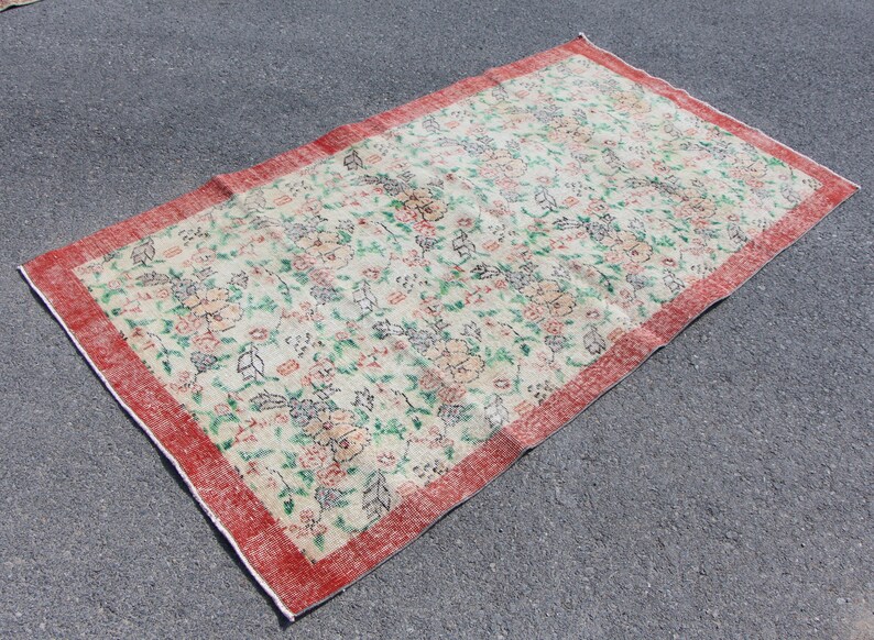Puede incluir: Una alfombra floral vintage con fondo crema y borde rojo. La alfombra presenta un patr&oacute;n repetitivo de flores y hojas en tonos verdes, rosas y marrones.
