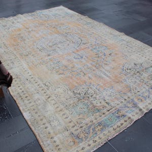 May include: A vintage rug with a faded floral pattern in shades of beige, blue, and green. The rug has a distressed look and is made of wool.