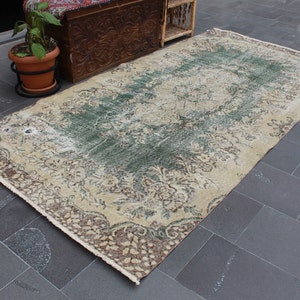 May include: A vintage rug with a cream background and a faded green and brown floral pattern. The rug has a distressed look and is perfect for adding a touch of bohemian style to any room.