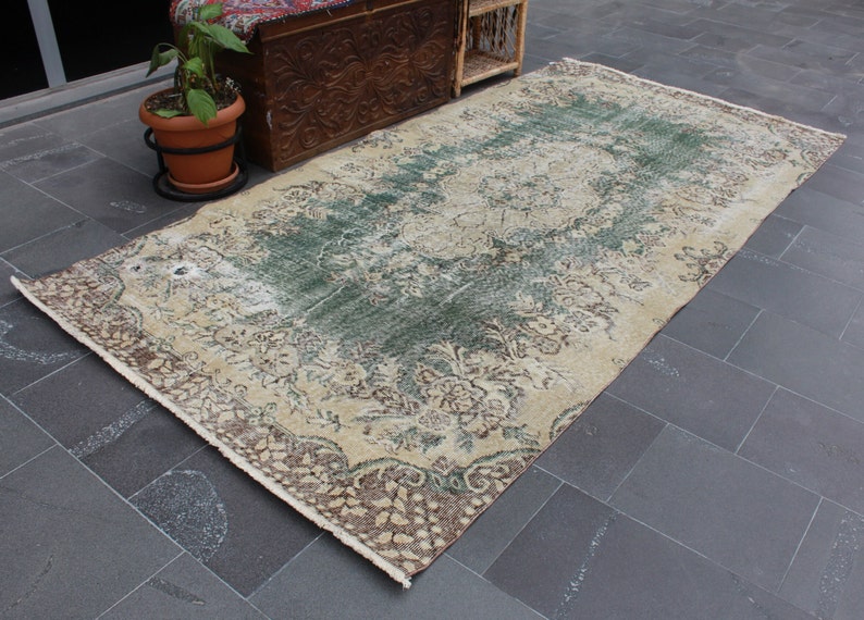 May include: A vintage rug with a cream background and a faded green and brown floral pattern. The rug has a distressed look and is perfect for adding a touch of bohemian style to any room.