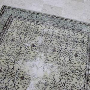 Puede incluir: Una alfombra vintage con un patr&oacute;n floral descolorido en tonos verdes, marrones y blancos. La alfombra tiene un aspecto desgastado y deteriorado, con algunas zonas que muestran signos de desgaste.