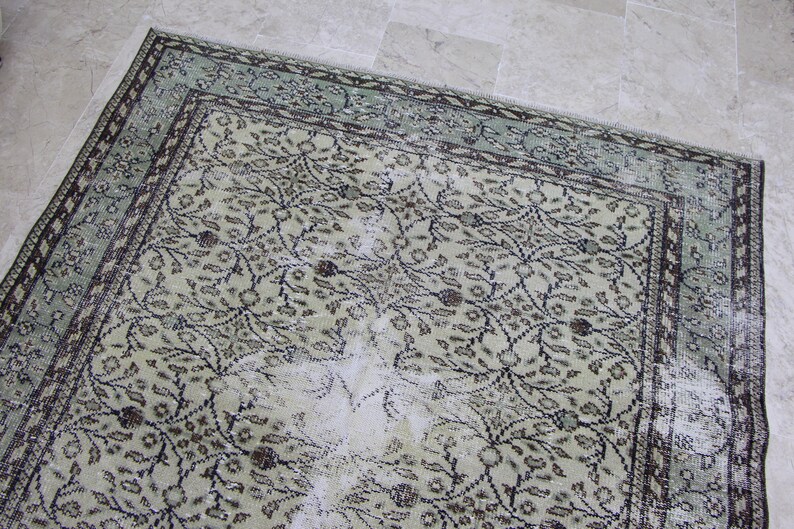 Puede incluir: Una alfombra vintage con un patr&oacute;n floral descolorido en tonos verdes, marrones y blancos. La alfombra tiene un aspecto desgastado y deteriorado, con algunas zonas que muestran signos de desgaste.