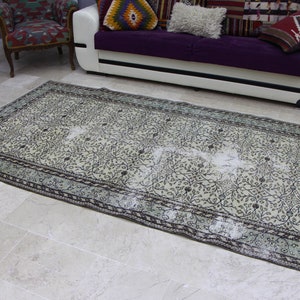 Puede incluir: Una alfombra vintage con estampado floral, fondo beige claro y dise&ntilde;o floral verde oscuro y negro. La alfombra tiene un borde azul claro con un patr&oacute;n floral verde oscuro y negro.