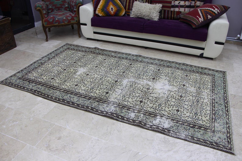 Puede incluir: Una alfombra vintage con estampado floral, fondo beige claro y dise&ntilde;o floral verde oscuro y negro. La alfombra tiene un borde azul claro con un patr&oacute;n floral verde oscuro y negro.