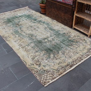 May include: A vintage rug with a cream background and a faded green and brown floral pattern. The rug has a fringed edge.