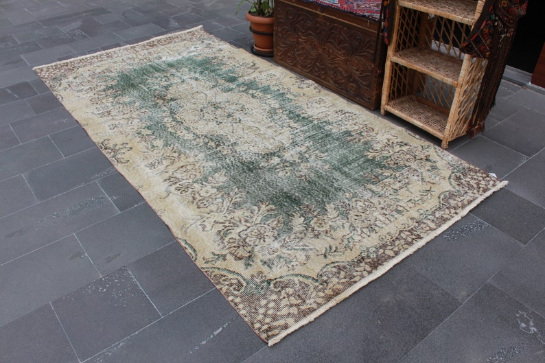 May include: A vintage rug with a cream background and a faded green and brown floral pattern. The rug has a fringed edge.