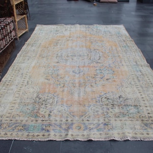 May include: A vintage rug with a faded floral pattern in shades of beige, blue, and pink. The rug has a fringed edge and a worn, distressed look.
