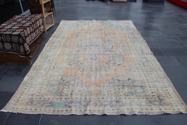 May include: A vintage rug with a faded floral pattern in shades of beige, blue, and pink. The rug has a fringed edge and a worn, distressed look.