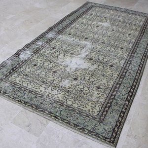 Puede incluir: Una alfombra vintage con fondo beige claro y un patr&oacute;n floral en tonos marrones y verdes. La alfombra tiene un aspecto descolorido y un borde verde claro.