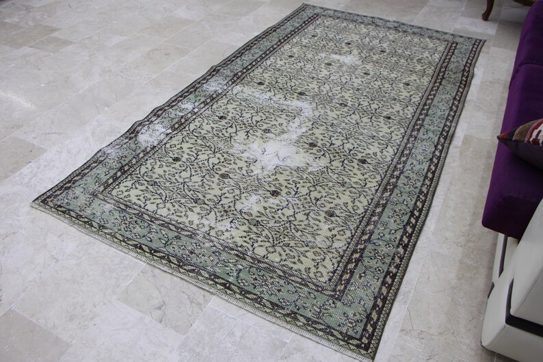 Puede incluir: Una alfombra vintage con fondo beige claro y un patr&oacute;n floral en tonos marrones y verdes. La alfombra tiene un aspecto descolorido y un borde verde claro.