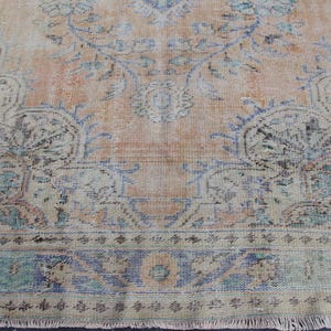 May include: A vintage rug with a faded floral pattern in shades of blue, pink, and beige. The rug has a fringed edge and a worn, distressed look.