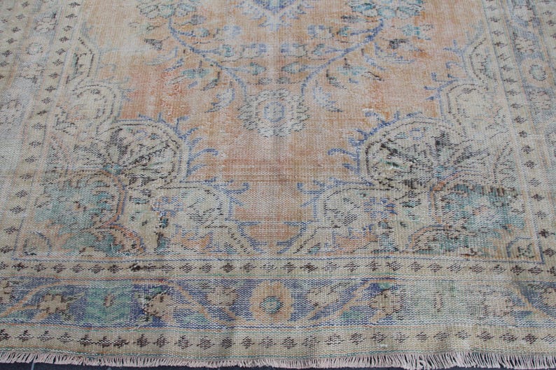May include: A vintage rug with a faded floral pattern in shades of blue, pink, and beige. The rug has a fringed edge and a worn, distressed look.
