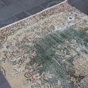 May include: A vintage rug with a faded floral pattern in shades of brown, cream, and green. The rug has a distressed look and is made of a soft, woven material.