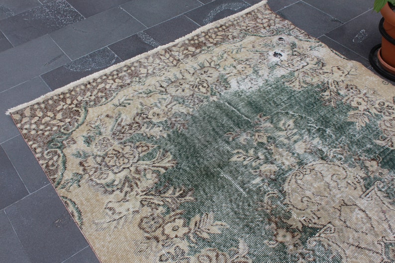 May include: A vintage rug with a faded floral pattern in shades of brown, cream, and green. The rug has a distressed look and is made of a soft, woven material.