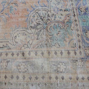 May include: A vintage rug with a faded floral pattern in shades of blue, pink, and beige. The rug has a fringed edge and a worn, distressed look.
