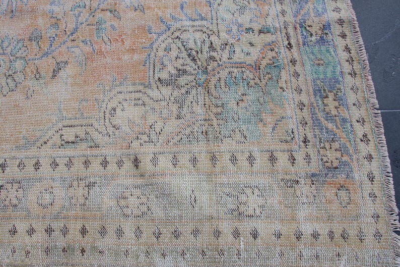 May include: A vintage rug with a faded floral pattern in shades of blue, pink, and beige. The rug has a fringed edge and a worn, distressed look.