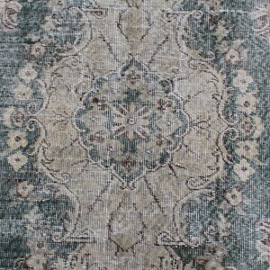 May include: A vintage rug with a faded floral pattern in shades of beige, brown, and green. The rug has a distressed look and a woven texture.