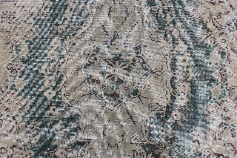May include: A vintage rug with a faded floral pattern in shades of beige, brown, and green. The rug has a distressed look and a woven texture.