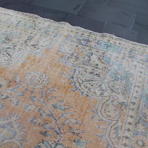 May include: A vintage rug with a faded, light brown background and a pattern of blue and white floral designs. The rug has a distressed, worn look, giving it a rustic and antique feel.