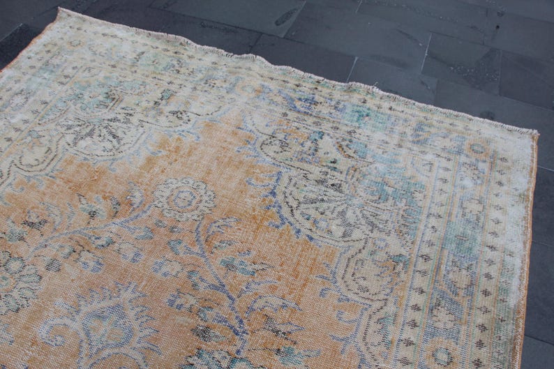 May include: A vintage rug with a faded, light brown background and a pattern of blue and white floral designs. The rug has a distressed, worn look, giving it a rustic and antique feel.