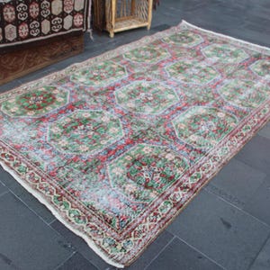 May include: A vintage rug with a cream background and a repeating pattern of red, green, and blue floral motifs. The rug has a worn and faded look, giving it a unique character.
