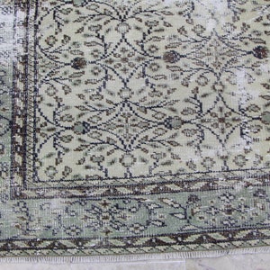 Puede incluir: Una alfombra vintage con un patr&oacute;n floral descolorido en verde y marr&oacute;n. La alfombra tiene un aspecto desgastado con un borde deshilachado.