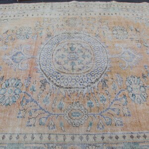 May include: A vintage rug with a light beige background and a faded floral pattern in shades of blue and green. The rug has a central medallion with a geometric design.