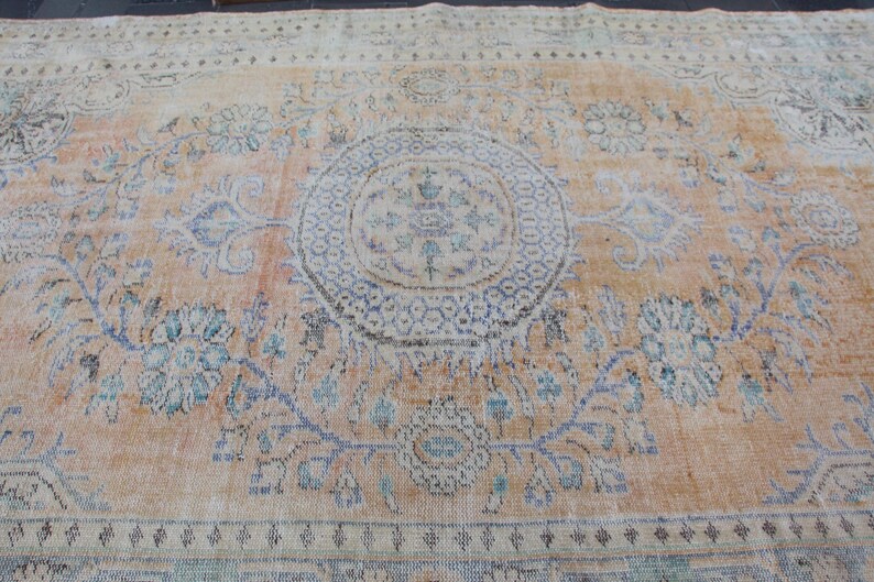 May include: A vintage rug with a light beige background and a faded floral pattern in shades of blue and green. The rug has a central medallion with a geometric design.