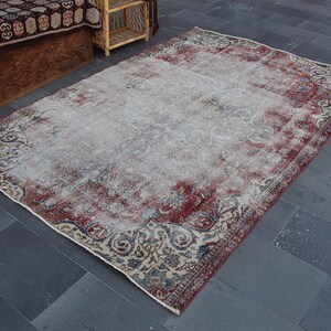 Puede incluir: Una alfombra rectangular, desgastada, con un aspecto vintage descolorido. La alfombra presenta un campo central de color beige claro con un borde rojo y azul oscuro. El diseño incluye patrones florales y geométricos.