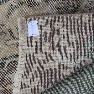 May include: Close-up of a beige and brown patterned rug with a fringe border. The rug is folded in half, revealing the back side, which is a brown and white pattern. A white tag with the number "MB8938" is attached to the rug.