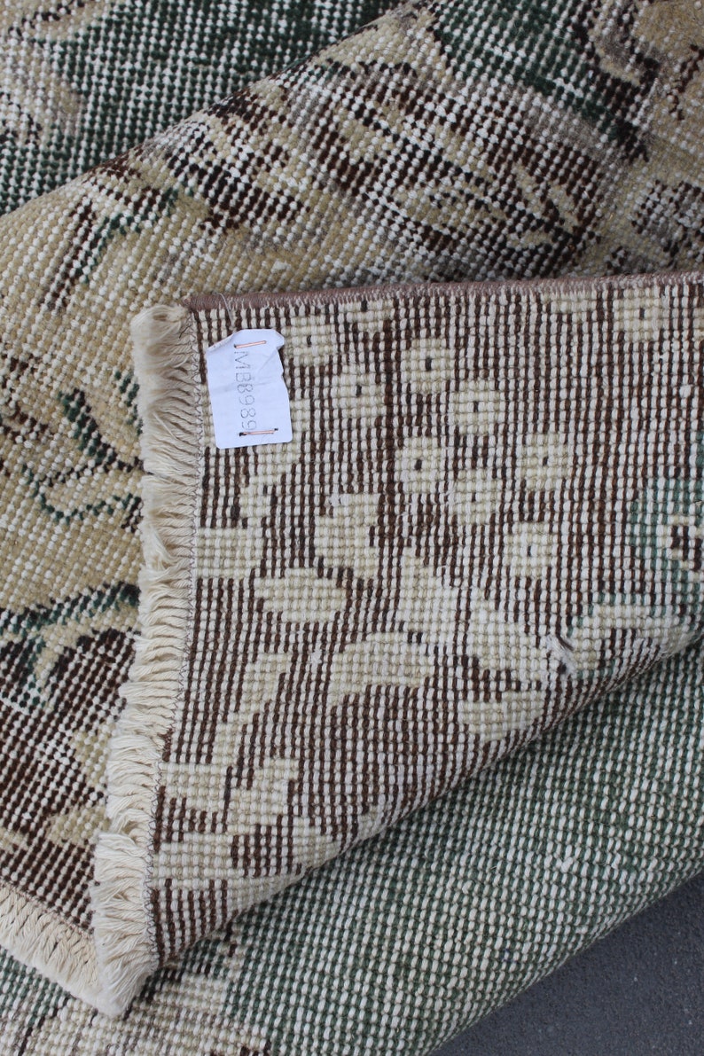 May include: Close-up of a beige and brown patterned rug with a fringe border. The rug is folded in half, revealing the back side, which is a brown and white pattern. A white tag with the number "MB8938" is attached to the rug.