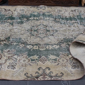 May include: A vintage rug with a faded floral pattern in shades of green, brown, and beige. The rug is rolled up on one side, revealing the underside.
