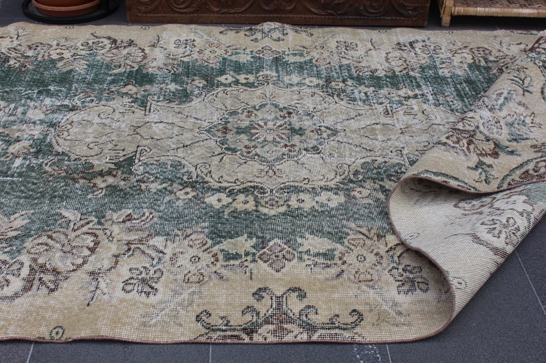 May include: A vintage rug with a faded floral pattern in shades of green, brown, and beige. The rug is rolled up on one side, revealing the underside.