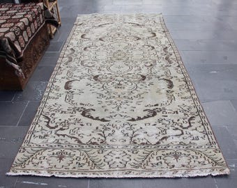 May include: A rectangular, vintage-style rug with an intricate, repeating pattern in shades of beige and brown. The rug features a central medallion design and ornate borders. The rug is placed on a dark gray tiled floor.