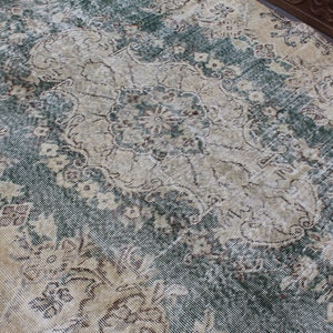 May include: A vintage rug with a faded floral pattern in shades of beige, brown, and green. The rug has a distressed look and is made of a soft, woven material.